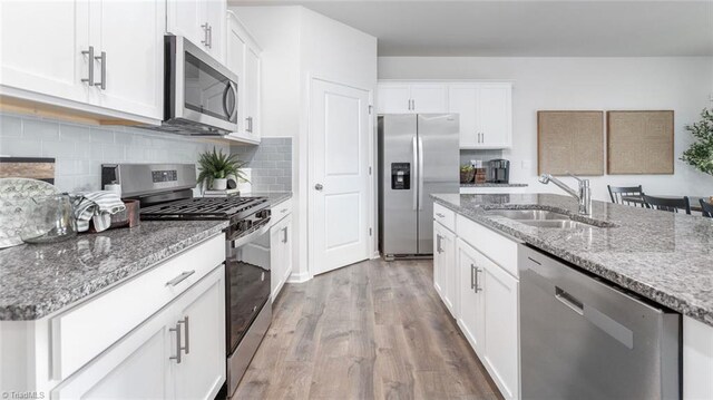 kitchen featuring a sink, appliances with stainless steel finishes, light wood-type flooring, light stone countertops, and tasteful backsplash