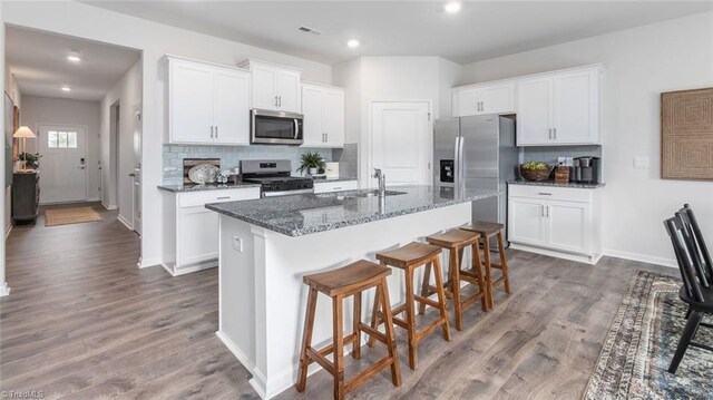 kitchen with wood finished floors, a kitchen island with sink, stainless steel appliances, a kitchen bar, and a sink
