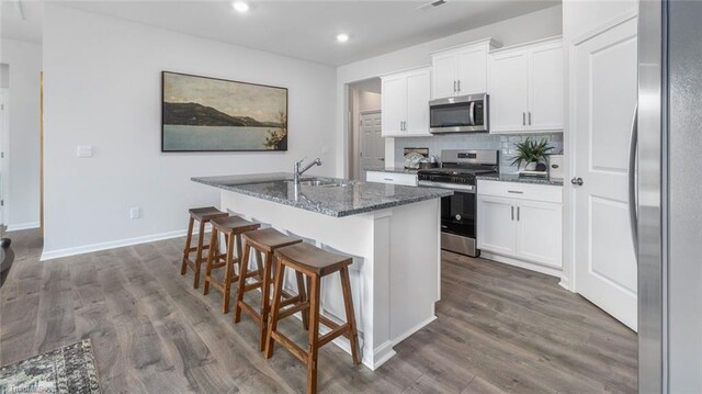 kitchen with stainless steel appliances, dark wood finished floors, a sink, and a center island with sink
