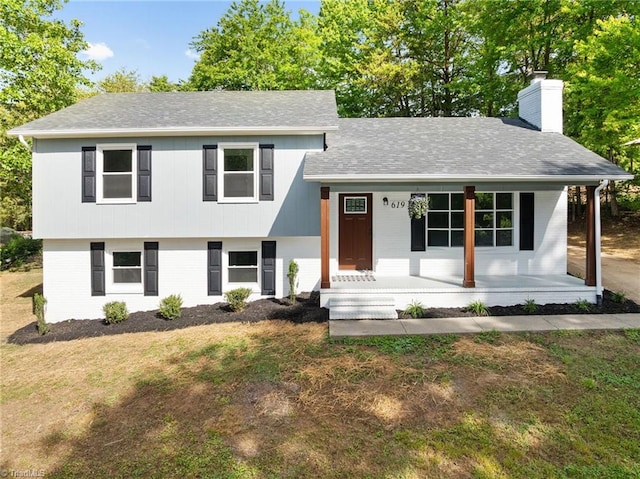 view of front of house with brick siding, a porch, a shingled roof, a chimney, and a front lawn