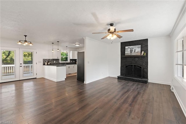 unfurnished living room featuring a textured ceiling, dark wood finished floors, ceiling fan, a fireplace, and baseboards