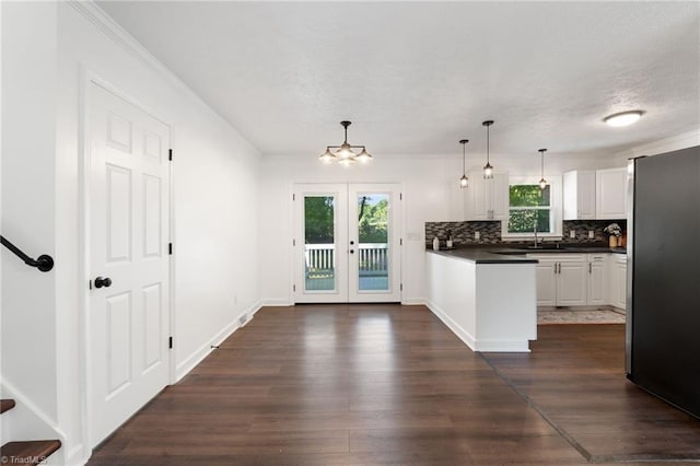 kitchen with dark countertops, freestanding refrigerator, backsplash, dark wood-style floors, and white cabinets