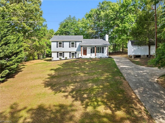split level home with a chimney, a front yard, view of wooded area, and driveway