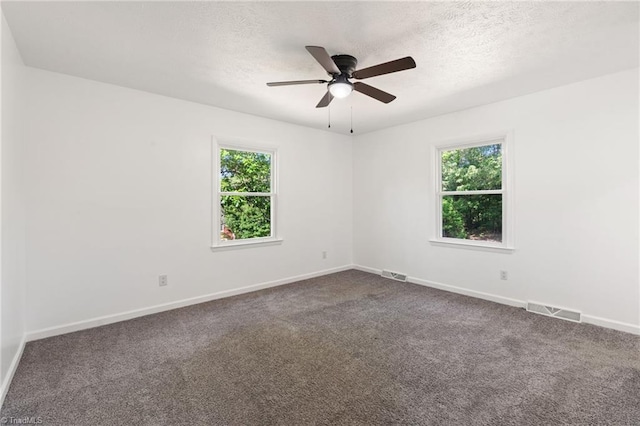 spare room featuring baseboards, dark carpet, a ceiling fan, and a textured ceiling