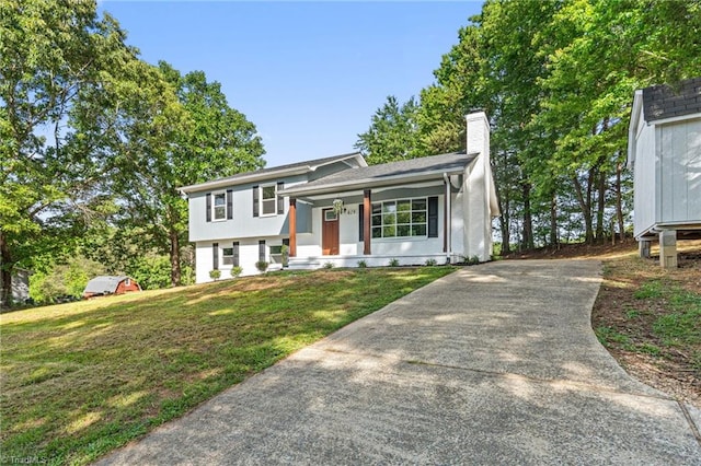 split level home with concrete driveway, a front yard, a porch, and a chimney
