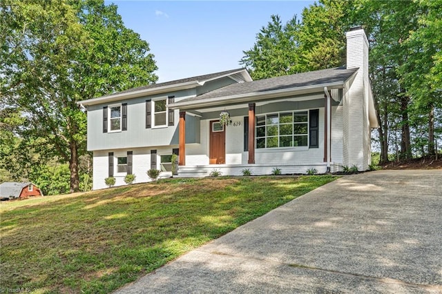 tri-level home featuring brick siding, a chimney, a front lawn, covered porch, and concrete driveway