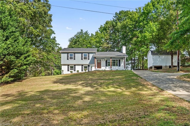 split level home with a chimney, a front lawn, covered porch, and driveway