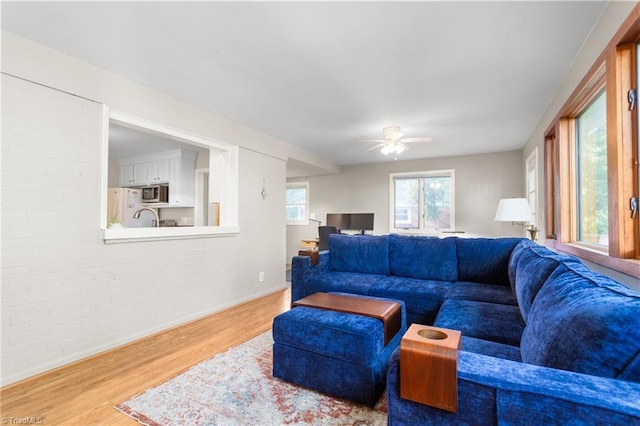 2909 Shamrock Dr, Greensboro, NC 27408 - living room featuring brick wall, wood finished floors, a ceiling fan, and baseboards