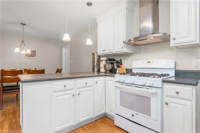 2909 Shamrock Dr, Greensboro, NC 27408 - kitchen featuring white gas range, wall chimney exhaust hood, a peninsula, dark countertops, and white cabinets