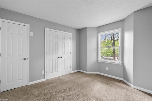 unfurnished bedroom with carpet flooring, a textured ceiling, baseboards, and a closet