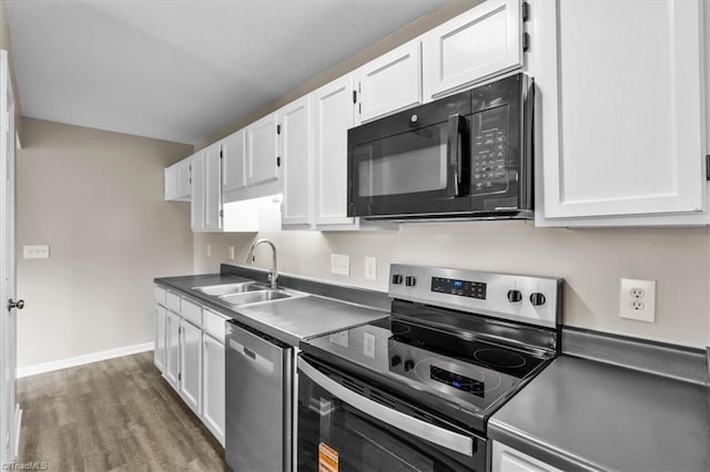 kitchen with wood finished floors, a sink, baseboards, white cabinets, and stainless steel appliances