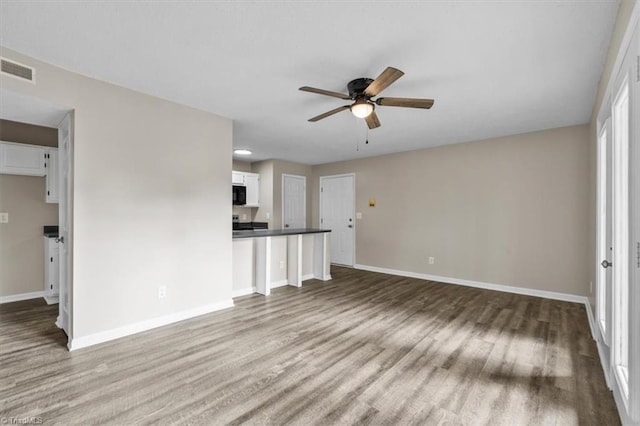 unfurnished living room with visible vents, a ceiling fan, baseboards, and wood finished floors