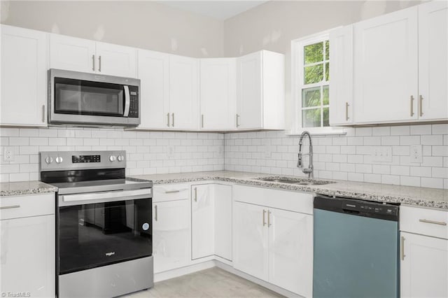 kitchen featuring a sink, stainless steel appliances, white cabinets, light stone countertops, and decorative backsplash