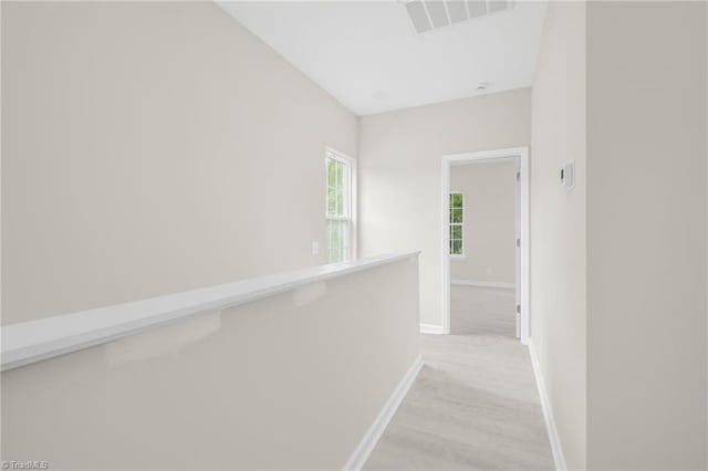 corridor with light wood-style floors, visible vents, and baseboards