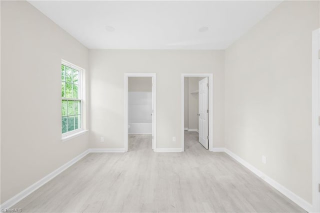 unfurnished bedroom with a walk in closet, baseboards, light wood-type flooring, and a closet