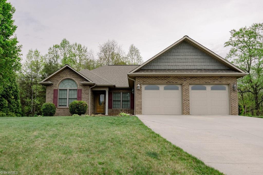 view of front of home featuring concrete driveway, roof with shingles, a front yard, brick siding, and a garage