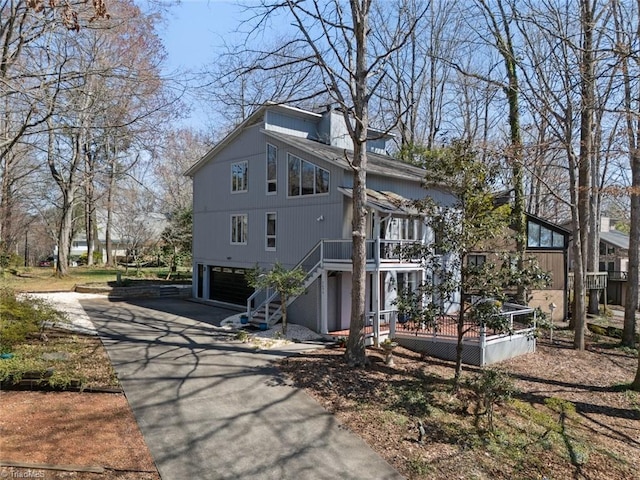 exterior space with stairway, driveway, a wooden deck, a chimney, and a garage