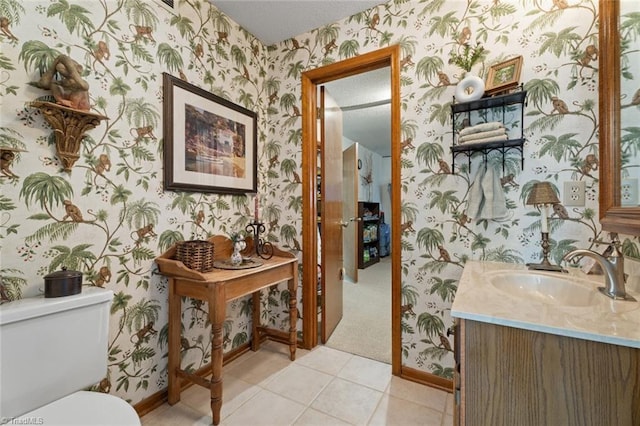 half bath with toilet, wallpapered walls, tile patterned flooring, baseboards, and vanity