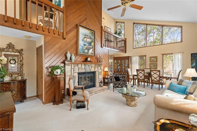 carpeted living room with a stone fireplace, ceiling fan, a high ceiling, and wooden walls