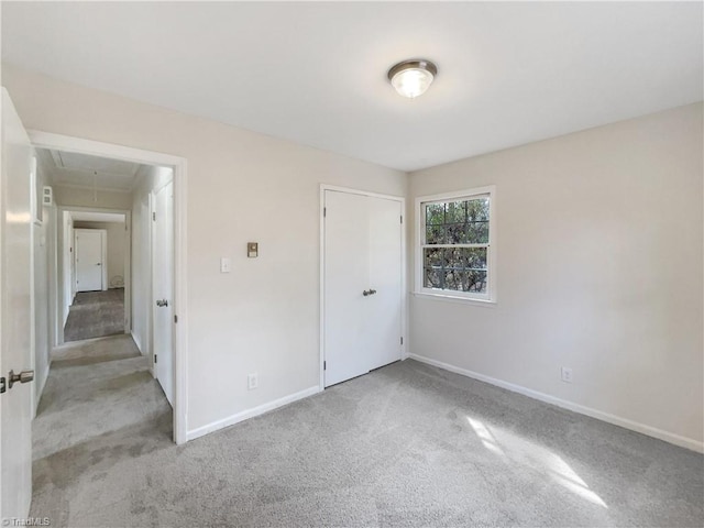 unfurnished bedroom featuring a closet, carpet, attic access, and baseboards