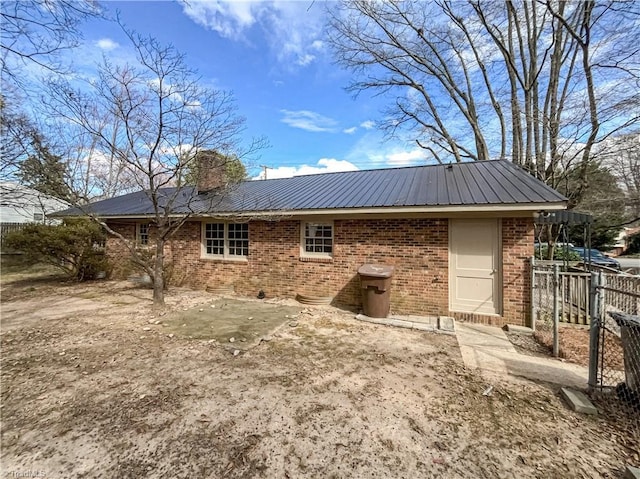 rear view of property with metal roof, brick siding, a chimney, and fence