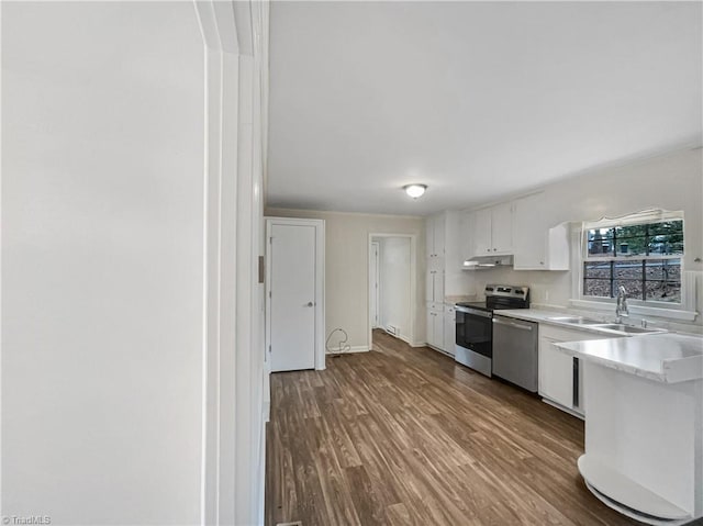 kitchen with appliances with stainless steel finishes, light countertops, under cabinet range hood, white cabinetry, and a sink