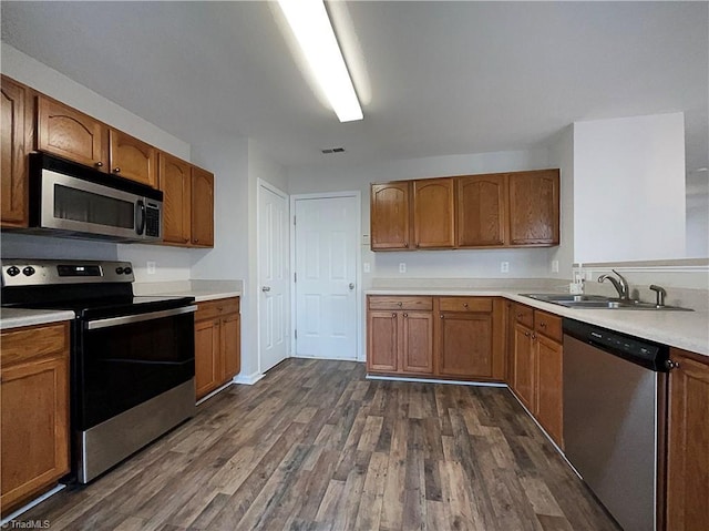 kitchen featuring dark wood-style flooring, a sink, light countertops, appliances with stainless steel finishes, and brown cabinetry