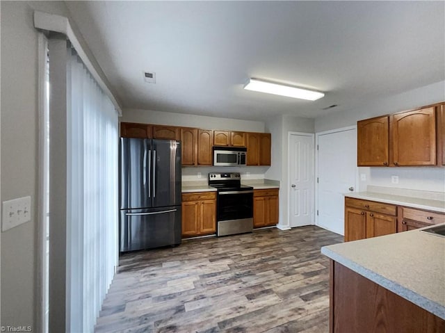 kitchen featuring visible vents, brown cabinets, wood finished floors, stainless steel appliances, and light countertops