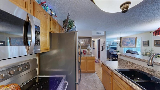 kitchen featuring appliances with stainless steel finishes, a sink, a textured ceiling, light tile patterned floors, and light countertops