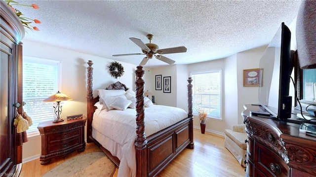 bedroom with multiple windows, light wood-style flooring, a textured ceiling, and baseboards