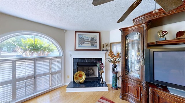 living area with a textured ceiling, light wood finished floors, a high end fireplace, ceiling fan, and baseboards