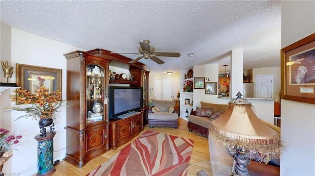 living room featuring a ceiling fan, a textured ceiling, and light wood finished floors