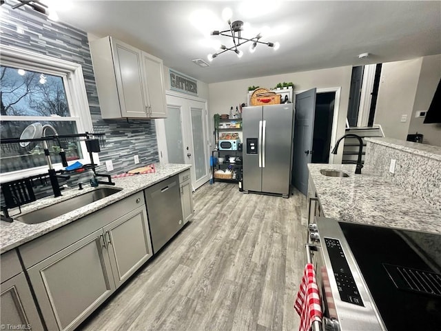 kitchen with light stone countertops, decorative backsplash, stainless steel appliances, an inviting chandelier, and gray cabinets