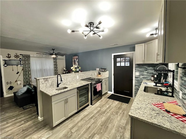 kitchen featuring kitchen peninsula, light stone countertops, beverage cooler, sink, and stainless steel range with electric cooktop