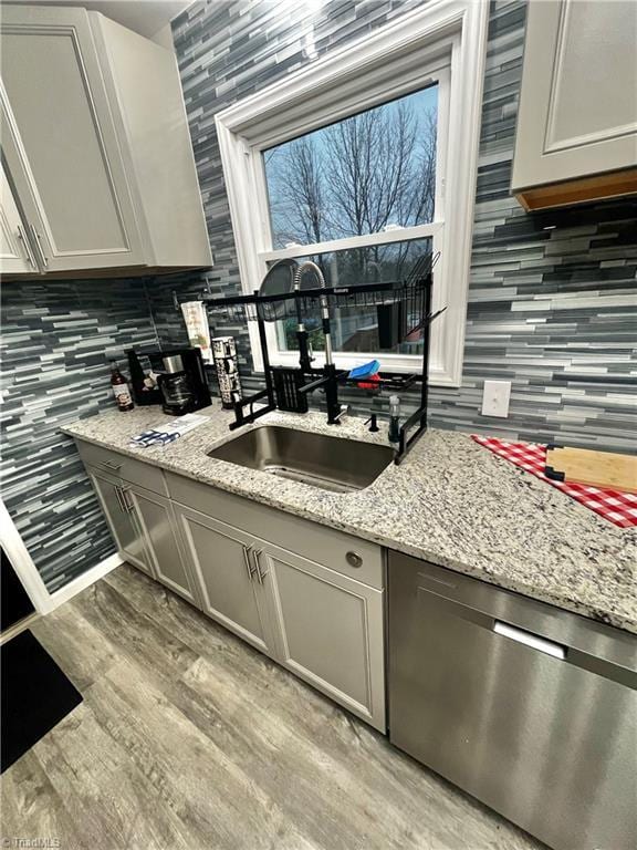 kitchen with gray cabinetry, dishwasher, sink, light hardwood / wood-style flooring, and light stone counters