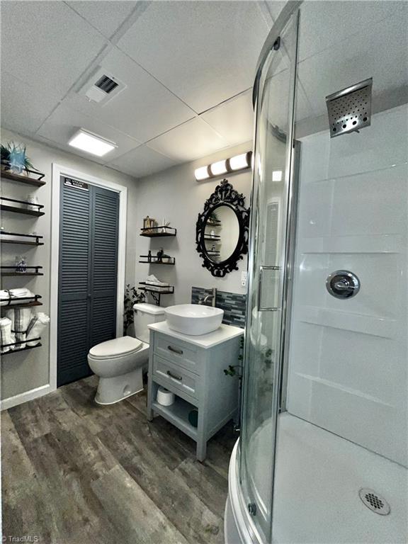 bathroom with a drop ceiling, toilet, vanity, a shower with shower door, and hardwood / wood-style flooring