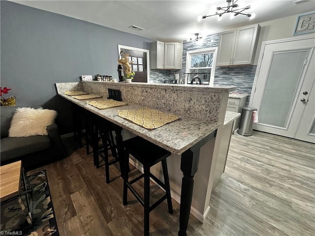 kitchen featuring a breakfast bar, light hardwood / wood-style flooring, decorative backsplash, light stone countertops, and kitchen peninsula