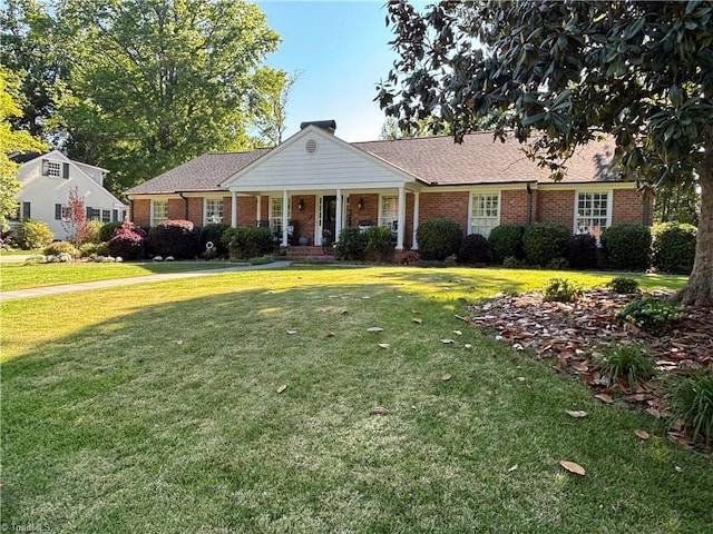view of front of home featuring covered porch, a chimney, a front yard, and brick siding
