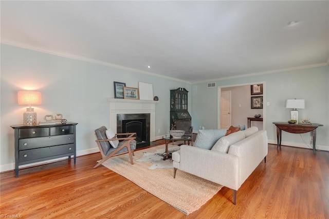 living area with crown molding, a high end fireplace, wood finished floors, and visible vents