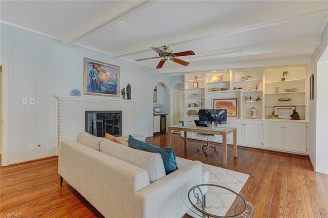 living room with arched walkways, a brick fireplace, wood finished floors, and beamed ceiling