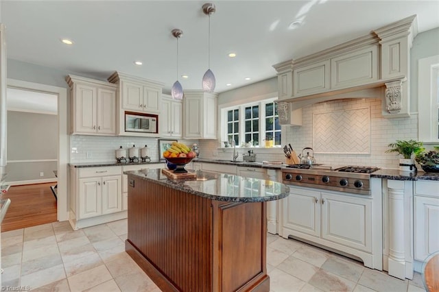 kitchen featuring white microwave, dark stone counters, tasteful backsplash, hanging light fixtures, and stainless steel gas stovetop