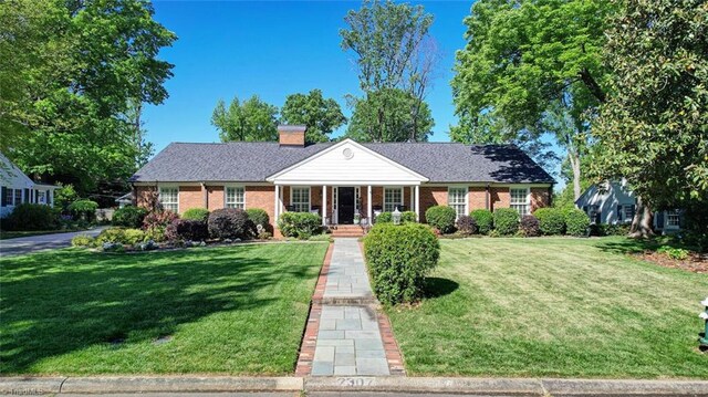 view of front facade featuring a chimney, brick siding, covered porch, and a front yard