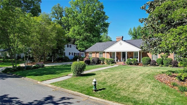 view of front of house featuring a chimney, a porch, brick siding, and a front yard