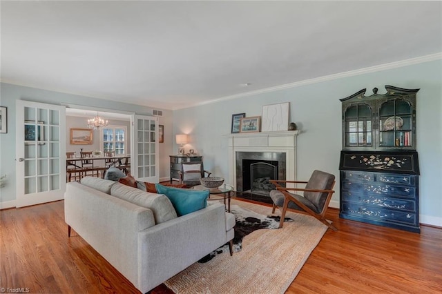 living room featuring crown molding, an inviting chandelier, a premium fireplace, wood finished floors, and visible vents