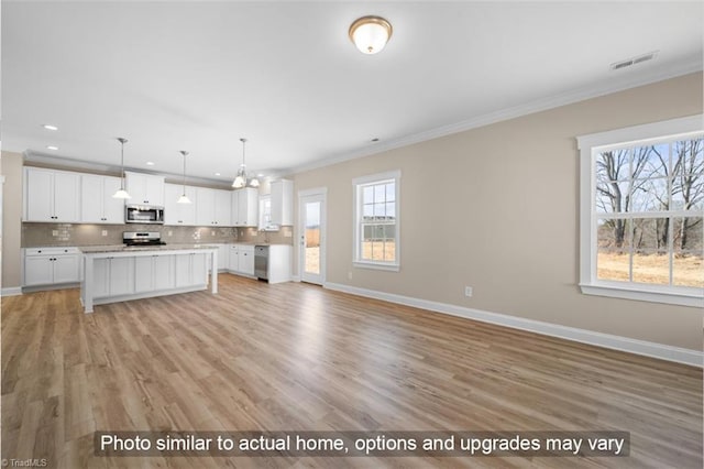 kitchen featuring tasteful backsplash, white cabinets, ornamental molding, open floor plan, and stainless steel appliances