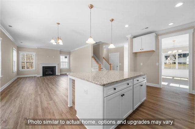 kitchen featuring a fireplace, an inviting chandelier, ornamental molding, white cabinets, and wood finished floors