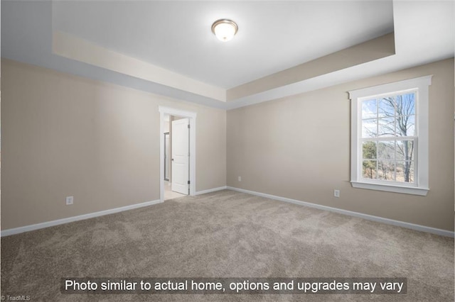 carpeted empty room featuring baseboards and a raised ceiling