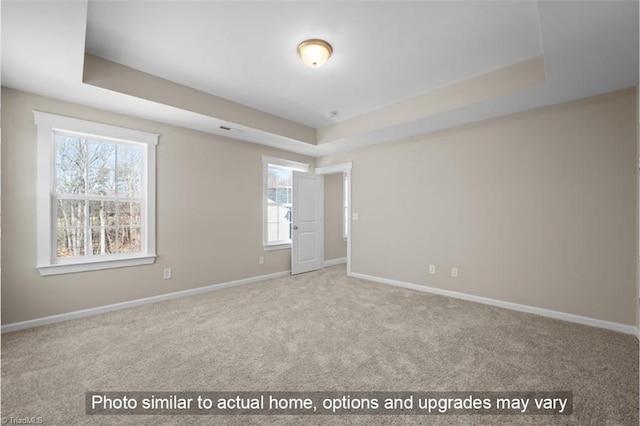 carpeted spare room featuring a tray ceiling, visible vents, and baseboards