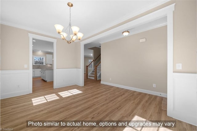 unfurnished dining area featuring ornamental molding, wainscoting, wood finished floors, and a notable chandelier