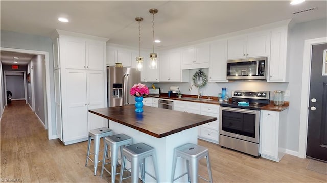 kitchen featuring white cabinetry, butcher block countertops, appliances with stainless steel finishes, sink, and a kitchen island